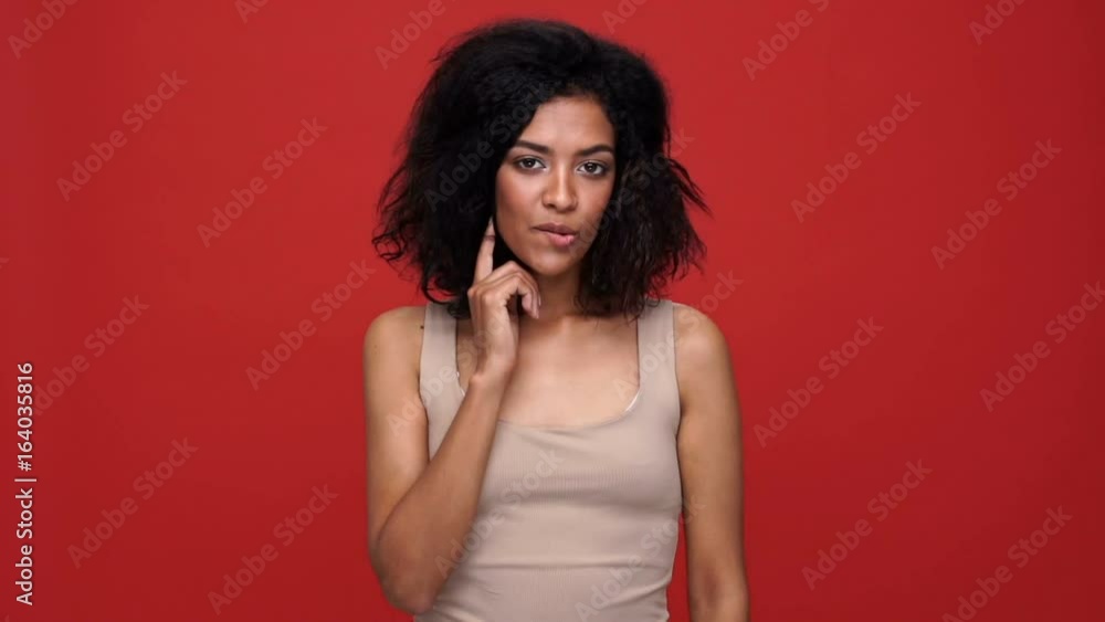 Young pretty african woman smiling and touching hair while bite lip over red background Young pretty african woman smiling and touching hair while bite lip over red background