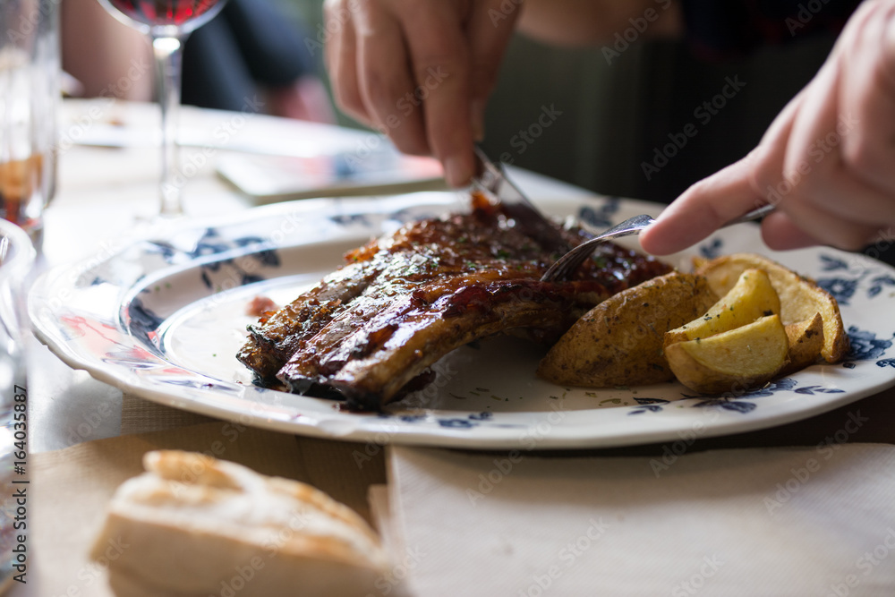 Man cutting pork ribs on the barbecue in restaurant, close up