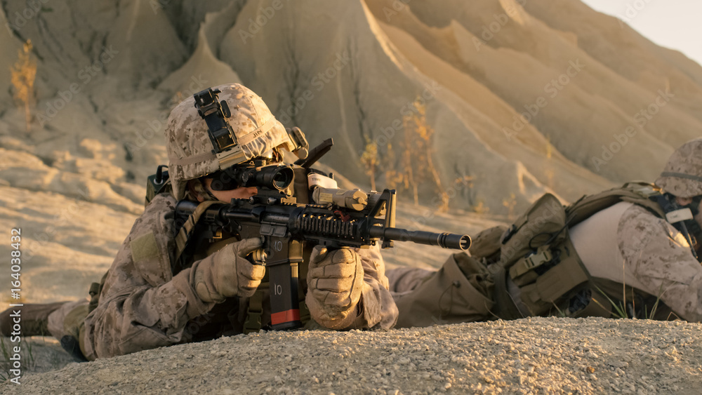 View on Soldier Lying Down on the Hill, Aiming through the Assault Rifle Scope in Desert Environment. View on Soldier Lying Down on the Hill, Aiming through the Assault Rifle Scope in Desert Environment.