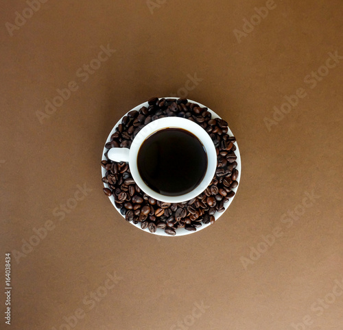 Hot black coffee in a white cup and coffee roast beans on brown paper in top of view.
