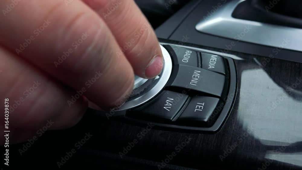 A man turns a knob and presses buttons on the gearshift box of a luxurious car - closeup