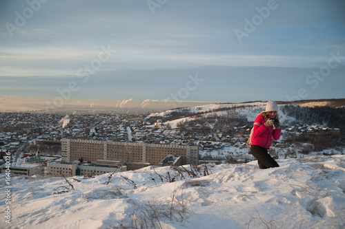 Girl tourist in a red jacket photographs the winter landscape on the camera. The tourist takes off the dawn in the morning. A girl in a gray hat takes off the morning city. Winter Saratov.