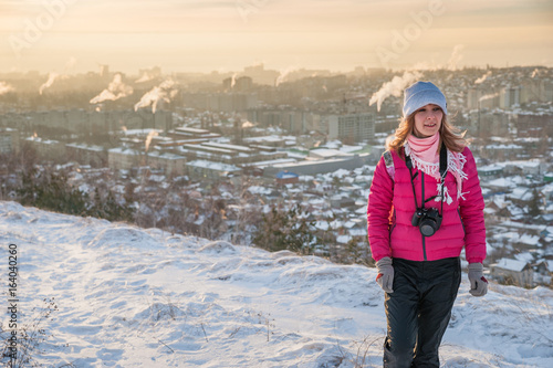 Girl tourist in a red jacket photographs the winter landscape on the camera. The tourist takes off the dawn in the morning. A girl in a gray hat takes off the morning city. Winter Saratov.