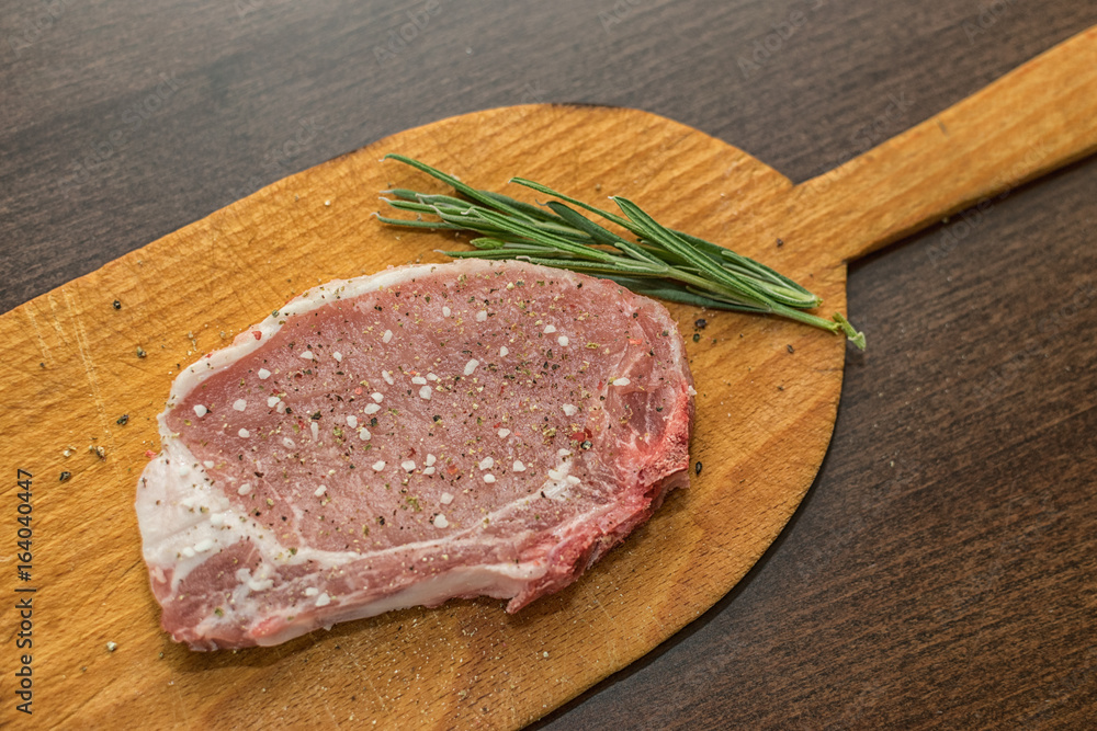 Raw pork steak with salt pepper ans rosemary on wooden board Raw pork steak with salt pepper ans rosemary on wooden board