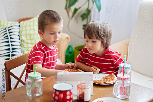 Two small children, boy brothers, eating breakfast at home, while watching cartoon