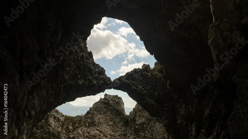 4 k timelapse shot looking up through the stone arch to the white moving clouds.  Piatra  Craiului Mountains, Romania. photo