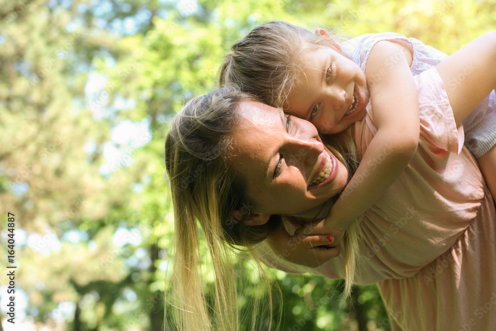 Mother and daughter outdoors in a meadow. Mother carrying her daughter on piggyback. Mother and daughter outdoors in a meadow. Mother carrying her daughter on piggyback.