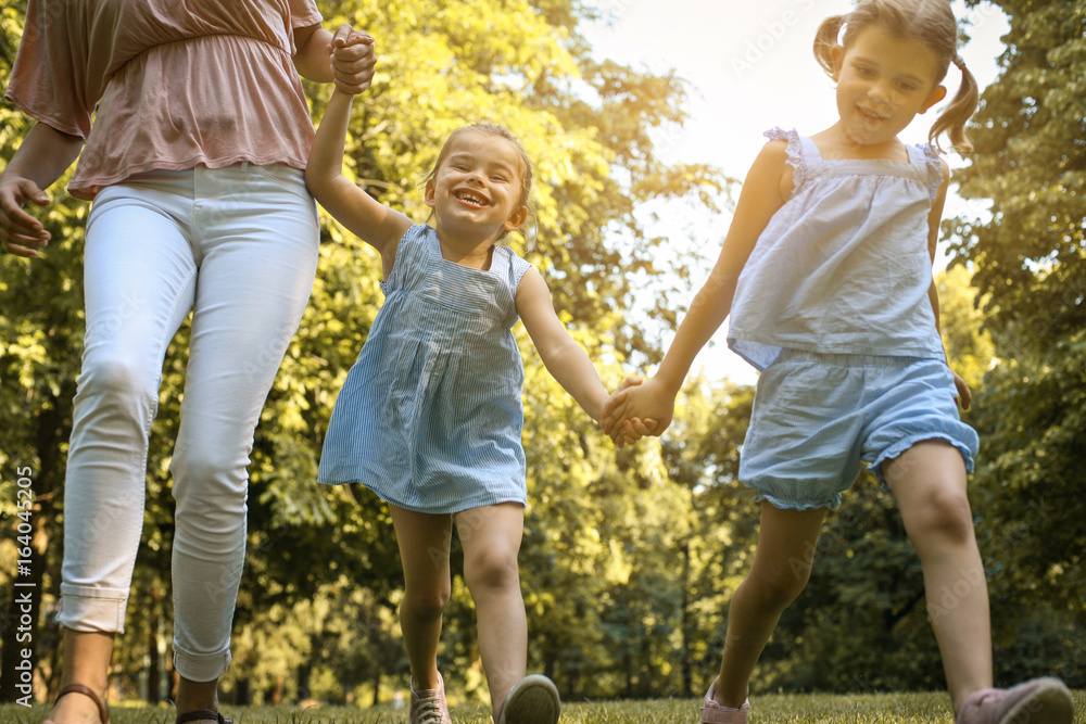 Fototapeta premium Mother with her daughter running trough meadow. Mother with two little daughter.