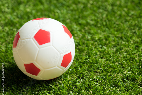 Toy red and white color football on artificial green grass background
