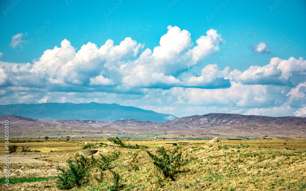 Desert landscape. Blue sky with white clouds. Summer steppe landscape. Hot desert with mountains view.