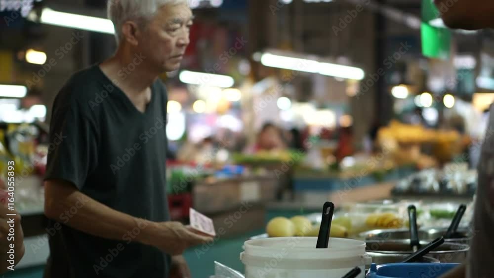 Asian senior man buying food at local market stall Asian senior man buying food at local market stall