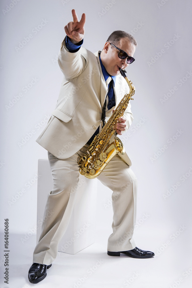 Fototapeta premium Saxophone only. Saxophonist. Caucasian man with a saxophone. Dressed in a white suit. The studio silhouette on a white background.