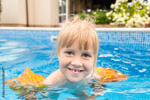 Little cute blonde girl swimming in a pool , wearing inflatable sleeves.  She is smiling and happy