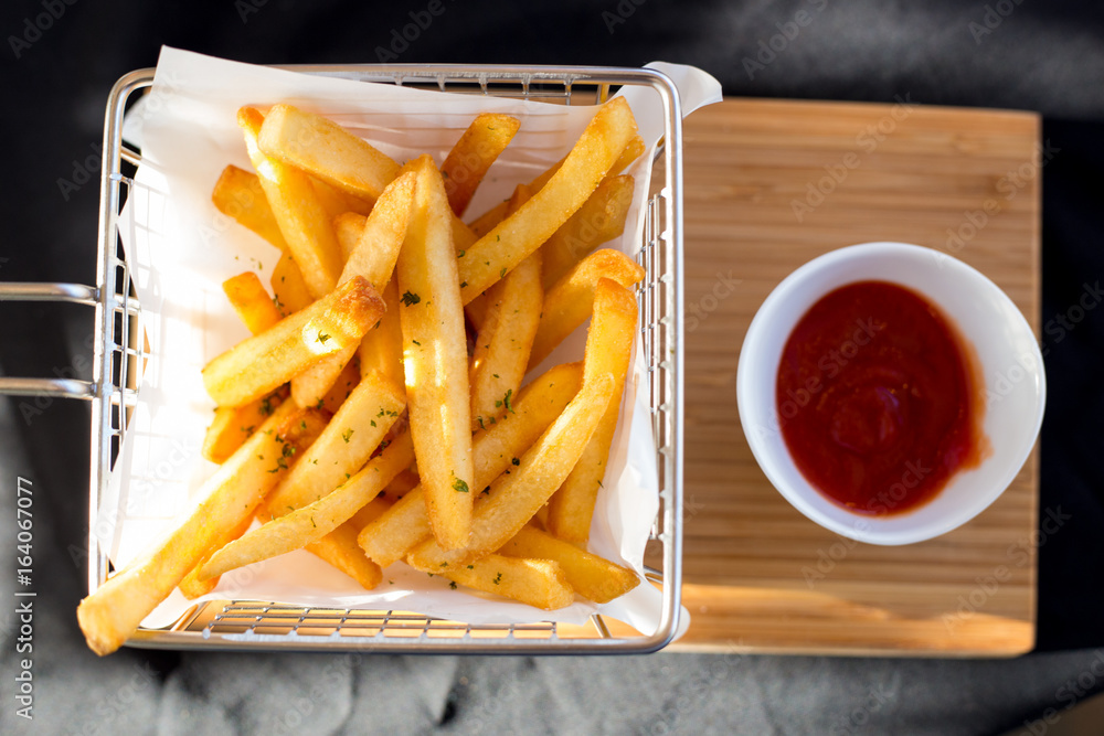 French fries in a metal basket with sauce on a wooden floor.