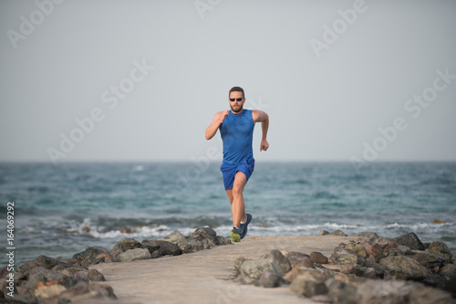 Runner boy in blue sportswear running along coast © Volodymyr