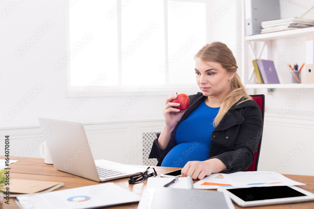 Pregnant woman eating apple in office copy space Pregnant woman eating apple in office copy space