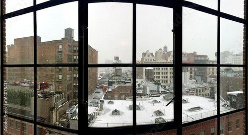 Idyllic urban winter scene in the cold SOHO streets of Manhattan (New York City, USA): Looking through the glass window seeing red brick houses with fireladders & white snow flakes on top of the roof