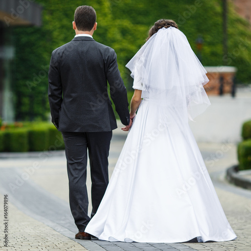 Look from behind at bride and groom walking on the backyard © IVASHstudio