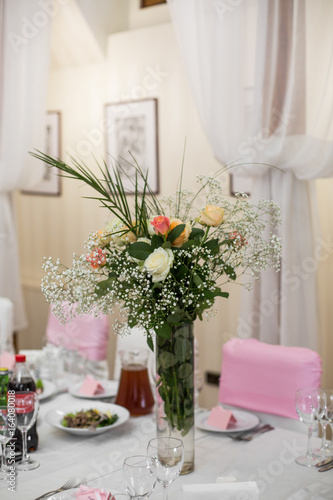 Rich bouquet of roses and greenery stands in the vase on dinner table