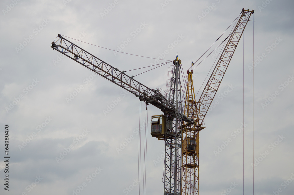Two construction cranes against a gray rainy sky background