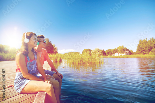 Φωτογραφία happy teenage couple with earphones on river berth