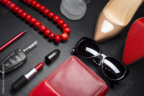 Woman accessories, shoes, jewelry, cosmetics, pen, bag in red color and other objects on leather black background, lifestyle, modern female concept, fashion industry 