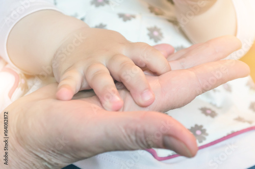 Child's hand of a baby on the hand of an adult person's palm. Concept of the relationship of grandmother and grandchildren