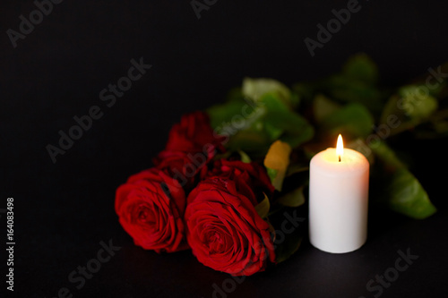 red roses and burning candle over black background