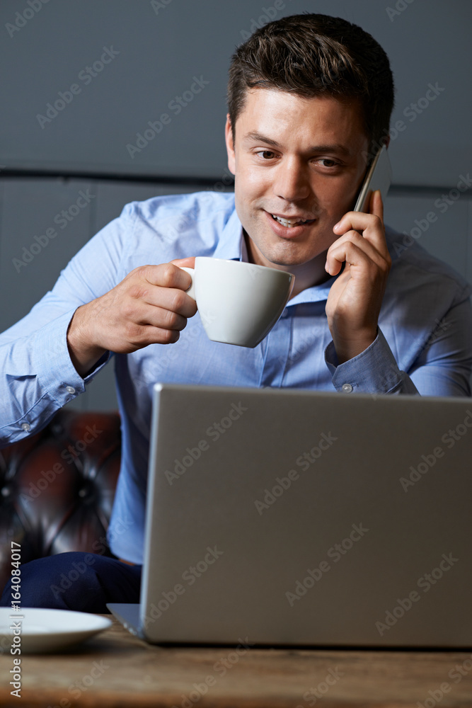 Businessman Talking On Mobile Phone Working On Laptop In Internet Cafe Businessman Talking On Mobile Phone Working On Laptop In Internet Cafe