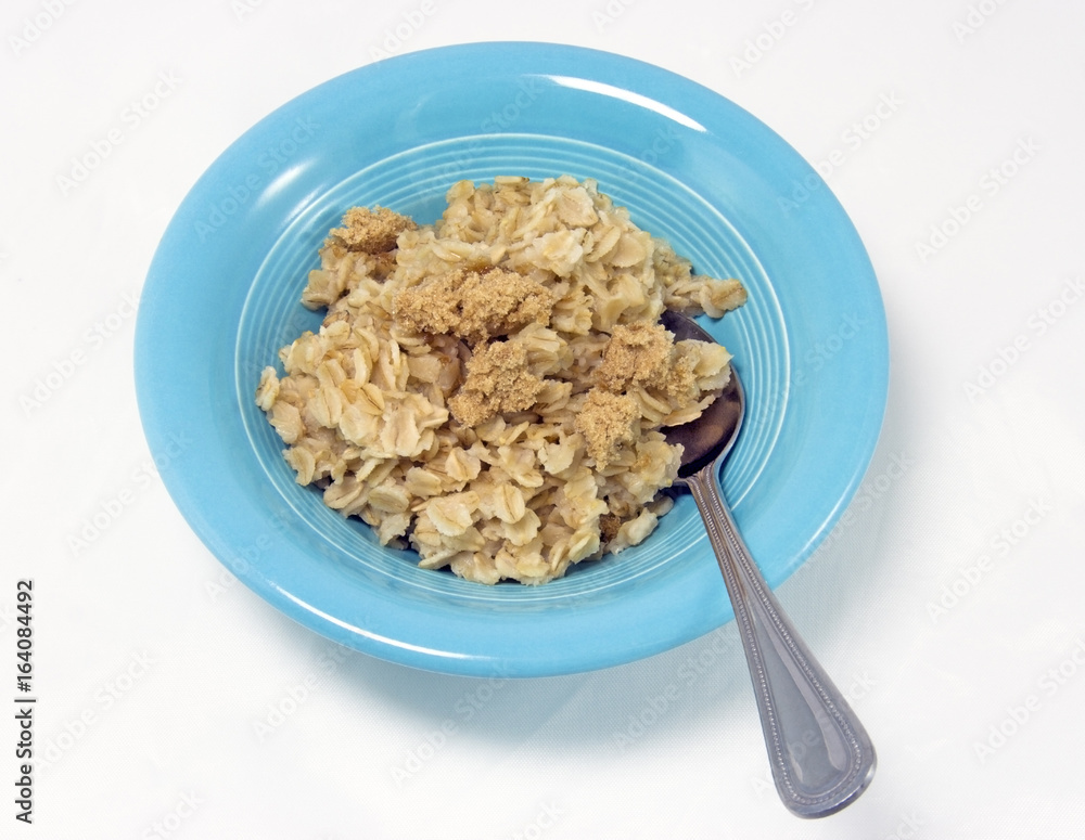Blue bowl filled with oatmeal and brown sugar with silver spoon. Isolated. Blue bowl filled with oatmeal and brown sugar with silver spoon. Isolated.