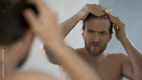 Middle-aged man looking in mirror at his bald patches, hair loss problem