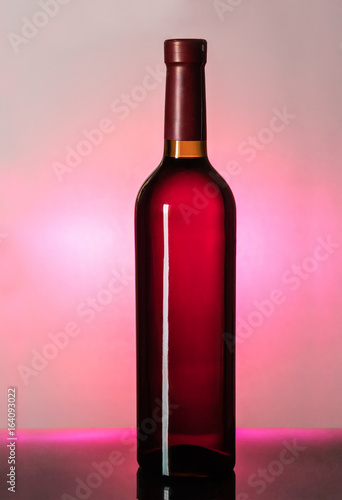 Closed wine bottle shot against the light on a pink background