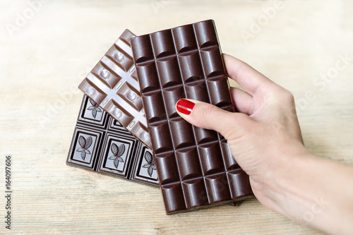 Bar of milk, black and porous chocolate in a woman's hand like a fan. Warm tone, wooden background photo