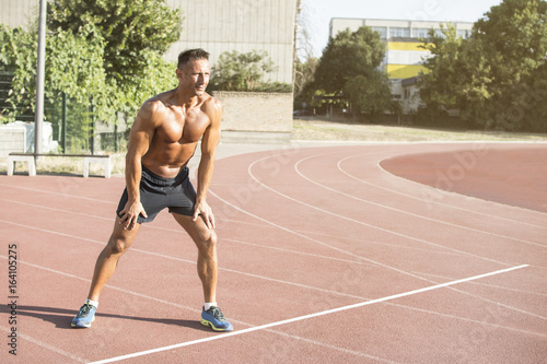Handsome middle aged man running on a running track. Healthy middle-aged athlete smiling during morning run. Shirtless man running.