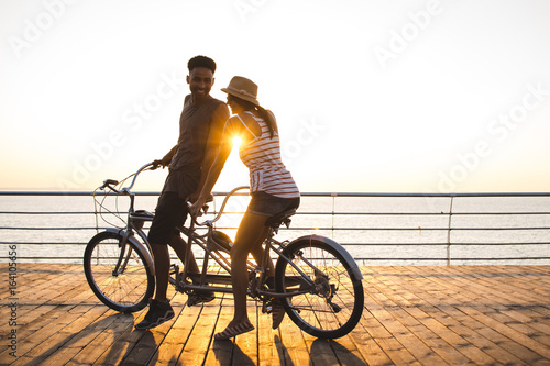 Foto Portrait of a mixed race couple riding on tandem bicycle outdoors near the sea