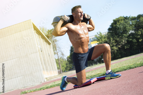 Handsome middle aged man working out on a running track. Healthy adult man doing step up with a heavy bag on the track. Tanned skin and shirtless middle-aged man.