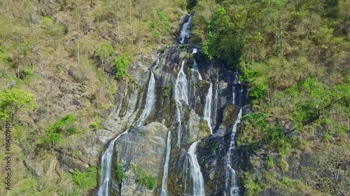 Drone Hangs above High Waterfall among Rocks in Highland photo