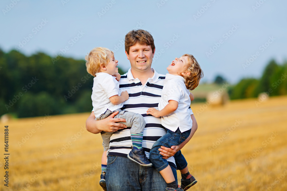 Father holding two children on arms on wheat field in summer Father holding two children on arms on wheat field in summer