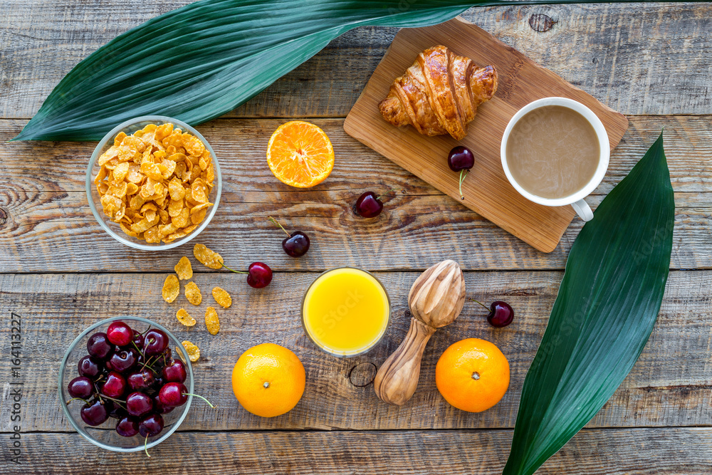 Light tasty breakfast. Muesli, oranges, cherry, french croissant and milky coffee on wooden table background top view Light tasty breakfast. Muesli, oranges, cherry, french croissant and milky coffee on wooden table background top view