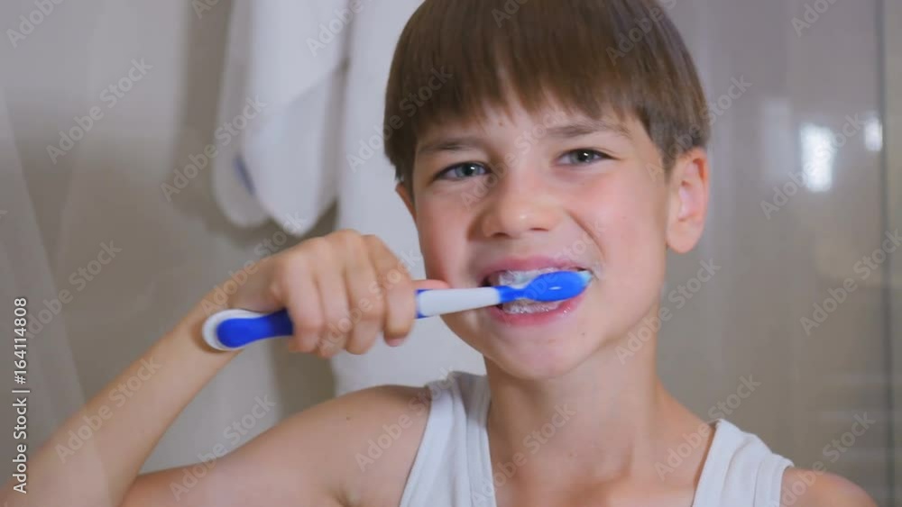 The child cleans his teeth. The boy is brushing his teeth in the bathroom. The child cleans his teeth. The boy is brushing his teeth in the bathroom.