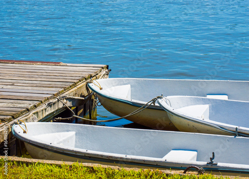 3 small rowboats tied to a weathered wooden dock on a Massachusetts lake photo