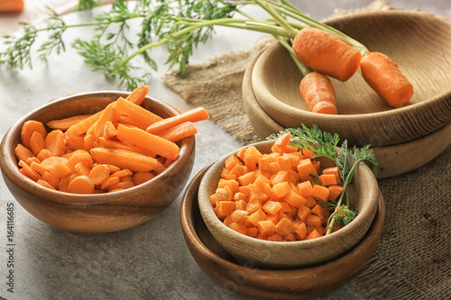 Different cuts of carrot in bowls on grey background