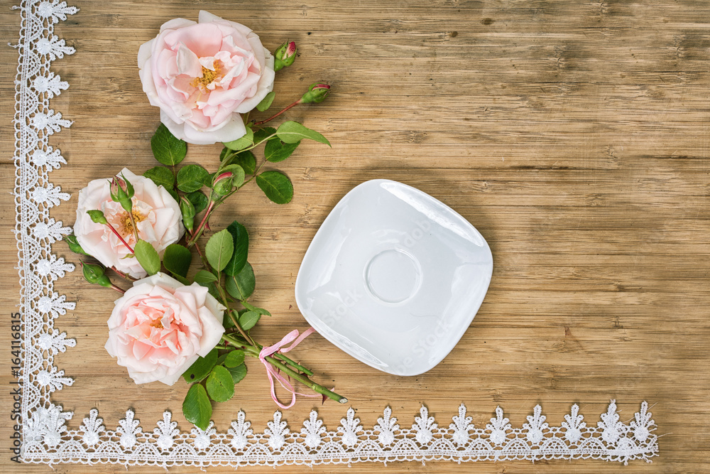 flat lay of pink roses with empty white sauser on a wooden table with lace frame and copy space for your text flat lay of pink roses with empty white sauser on a wooden table with lace frame and copy space for your text