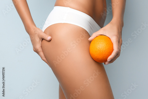 Young woman holding orange on light background. Cellulite problem concept photo