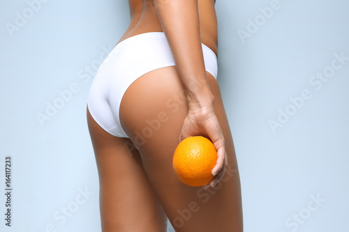 Young woman holding orange on light background. Cellulite problem concept