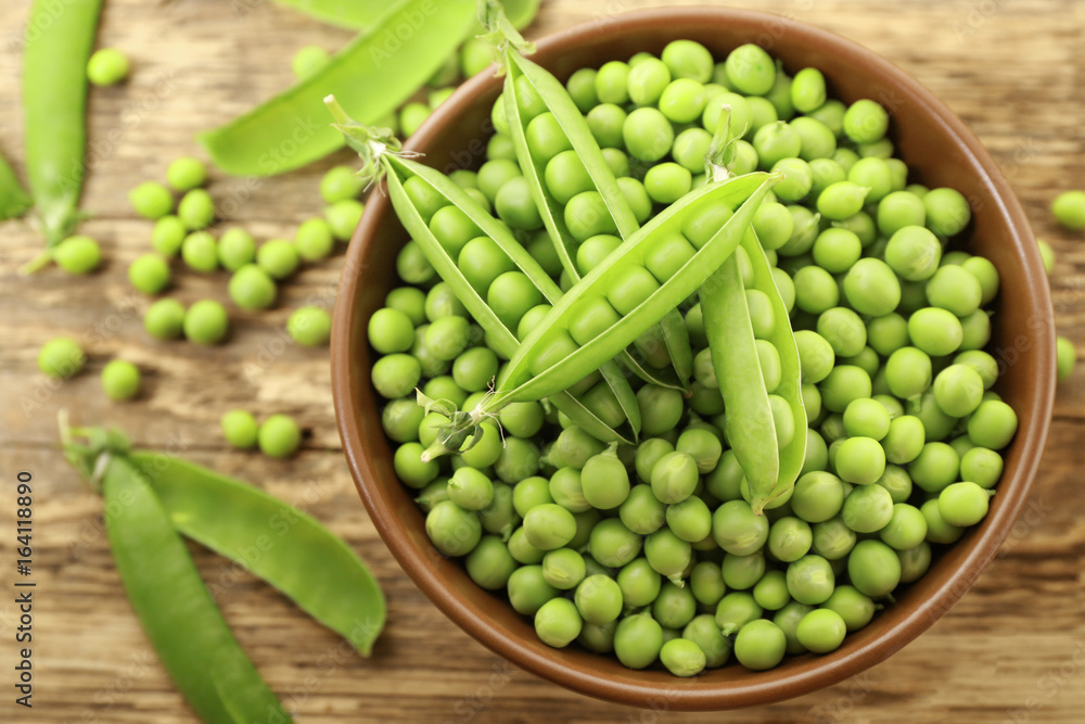 Bowl with fresh green peas on wooden background
