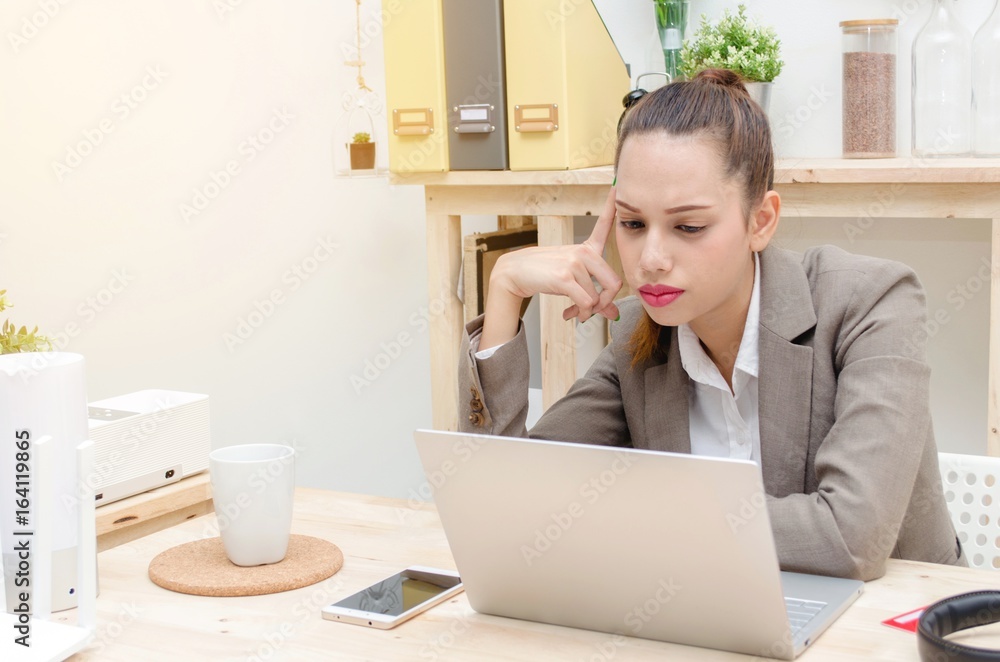 stressed asian young business woman beautiful smile working on laptop notebook computer on wood desk at office with alarm clock, headphone, smartphone, wireless router, document folder, soft focus stressed asian young business woman beautiful smile working on laptop notebook computer on wood desk at office with alarm clock, headphone, smartphone, wireless router, document folder, soft focus