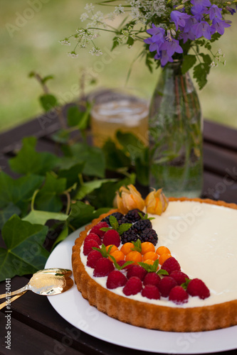 Summer berries and greek yogurt tart with honey on the dark table outside