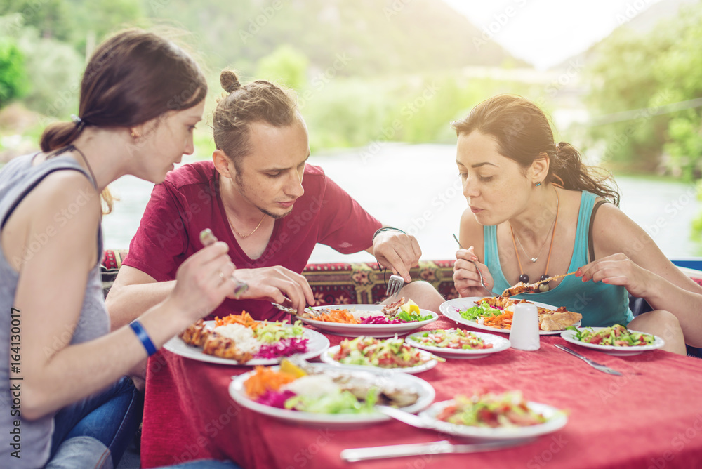 Young people are eating vegetables and fish outdoors in a cozy restaurant on the water, opens new kitchen Young people are eating vegetables and fish outdoors in a cozy restaurant on the water, opens new kitchen
