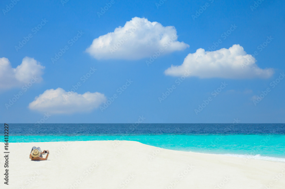 A woman lying and relaxing on a white sand beach with turquoise sea and blue sky in the Maldives.